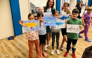Dzieci z panią prowadząca prezentują swoje rysunki o tematyce z rekinami