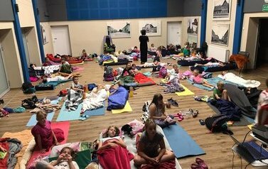 Dzieci leżą w śpiworach na dużej sali GOK-u